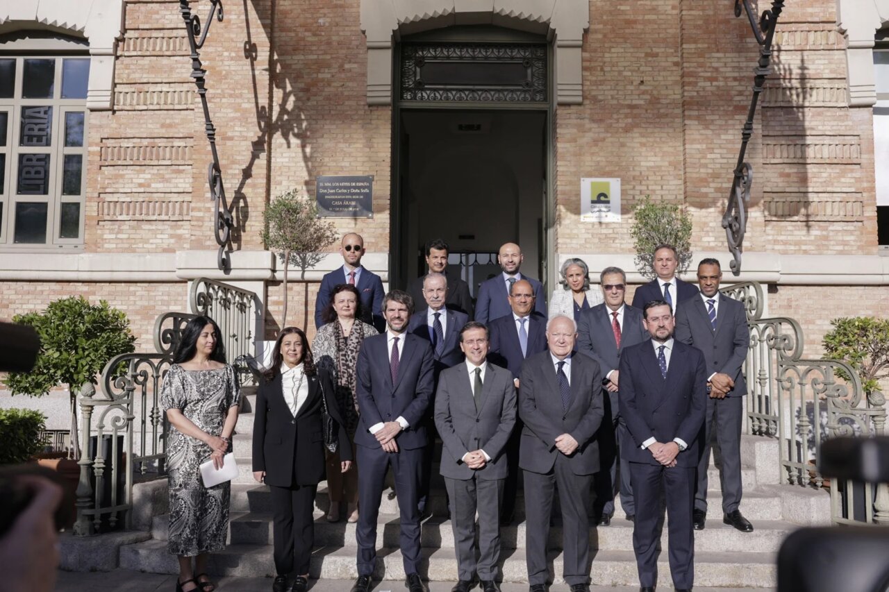 Group of formally dressed professionals posing for a group photo on the steps of a brick building outside a doorway.