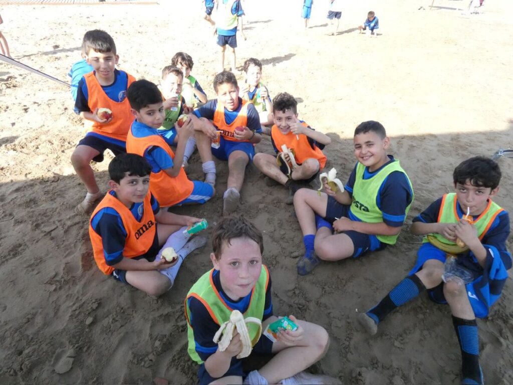 Niños disfrutando de una merienda tras jugar fútbol playa en la playa de San Lorenzo