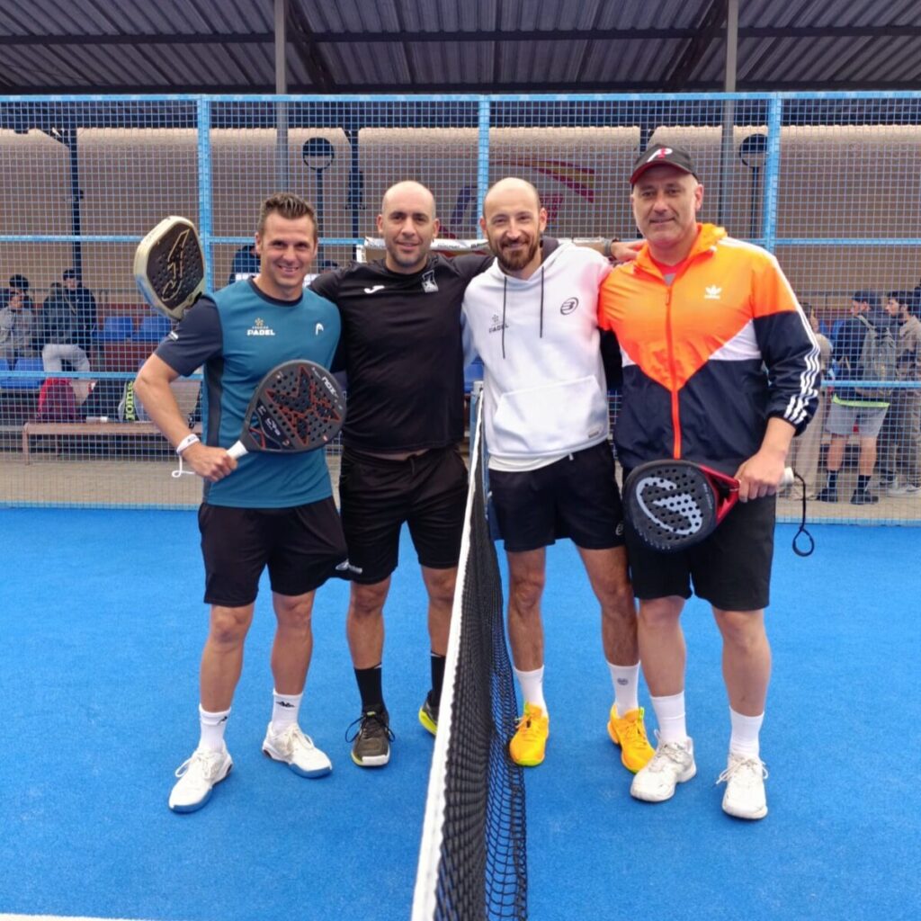 Four men stand together on a blue padel court, holding paddles and smiling at the net.