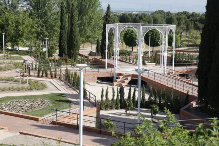 Public park with brick terraces, white metal arches, and winding paths among trees and shrubs to the center. ( informative )