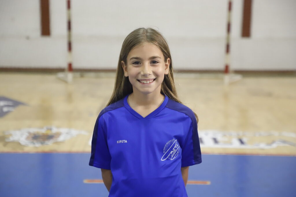 Niña sonriente con camiseta azul en una cancha de fútbol sala