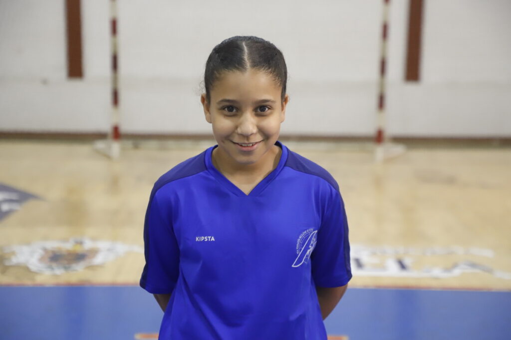 Niña sonriente con camiseta azul en una cancha de fútbol sala