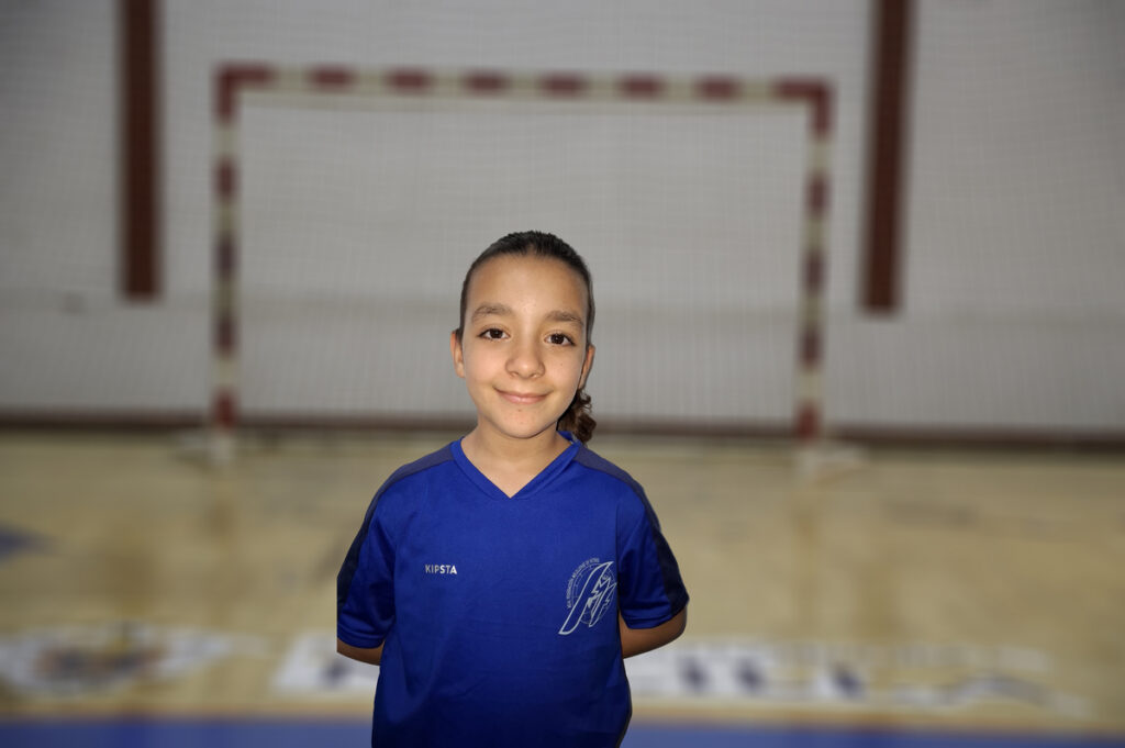 Niña sonriendo con camiseta azul en cancha de fútbol sala