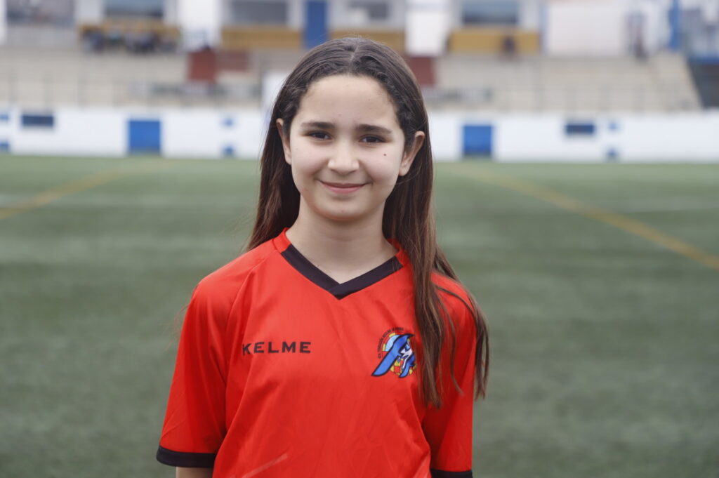 Niña sonriente en uniforme de fútbol rojo en campo de juego
