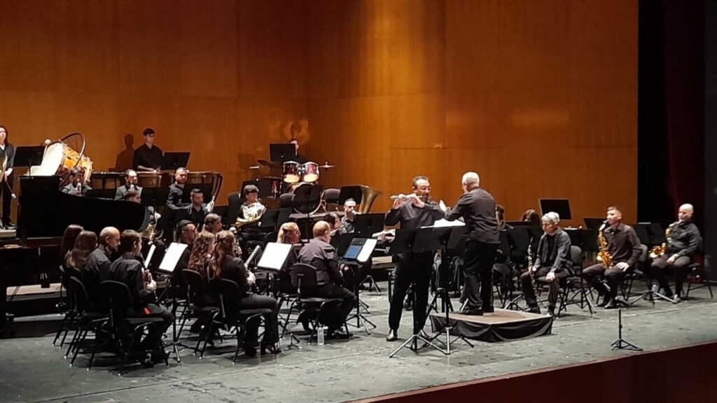 Full orchestra on a stage with a conductor in front, performing in a concert hall.
