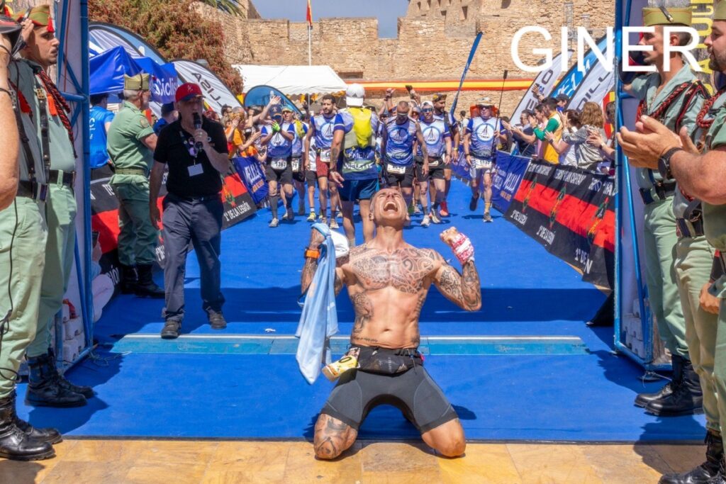 Corredor celebrando en la meta de una carrera con emoción y tatuajes visibles