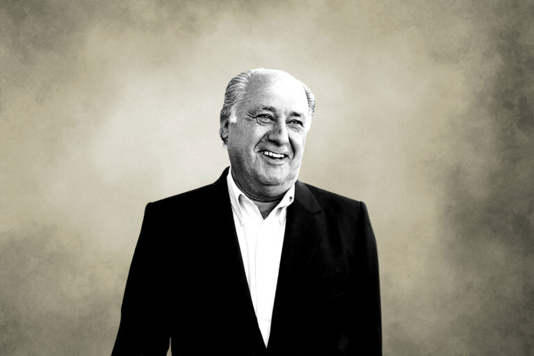 Smiling man in a dark suit and white shirt against a beige textured background.