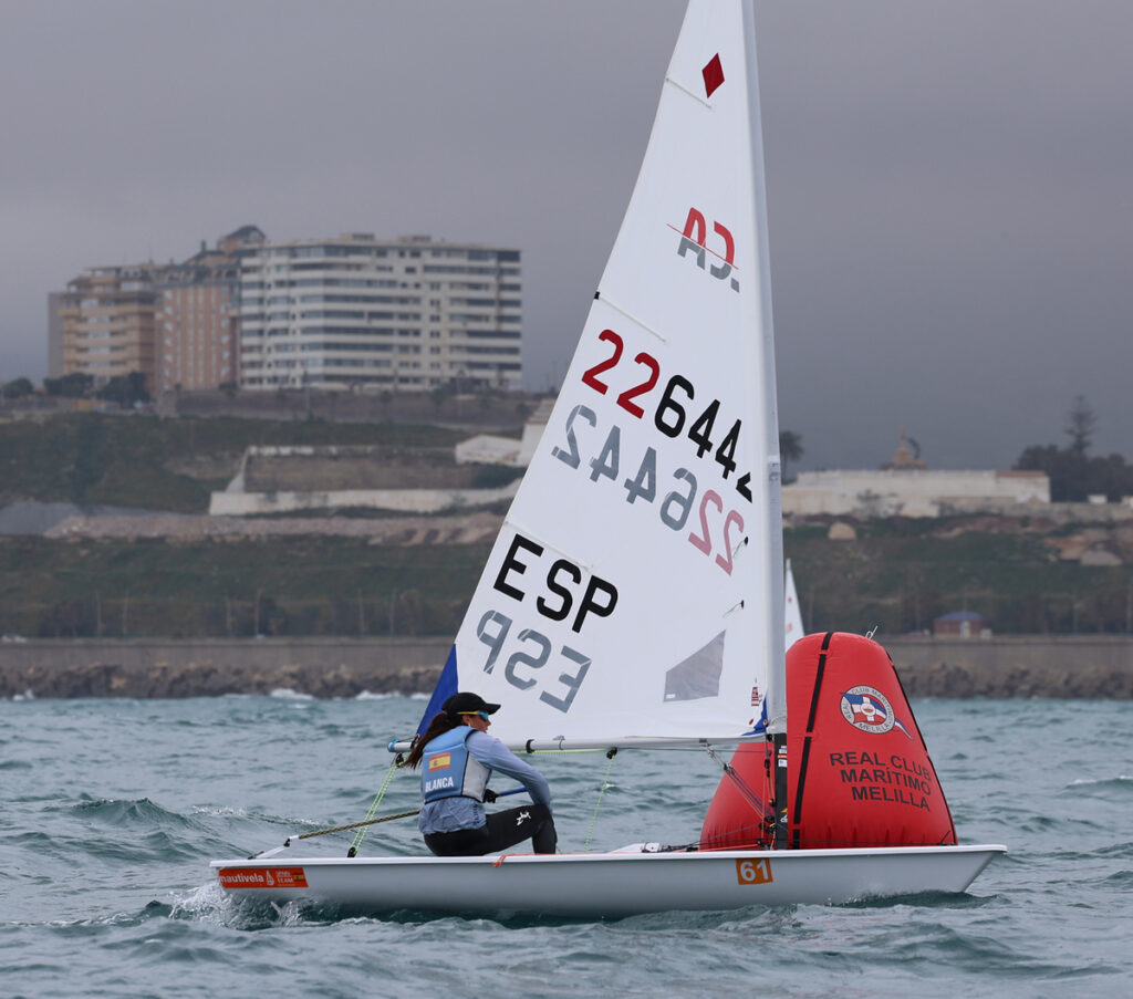 Regatista en competición de Ilca6 en Melilla con bandera española