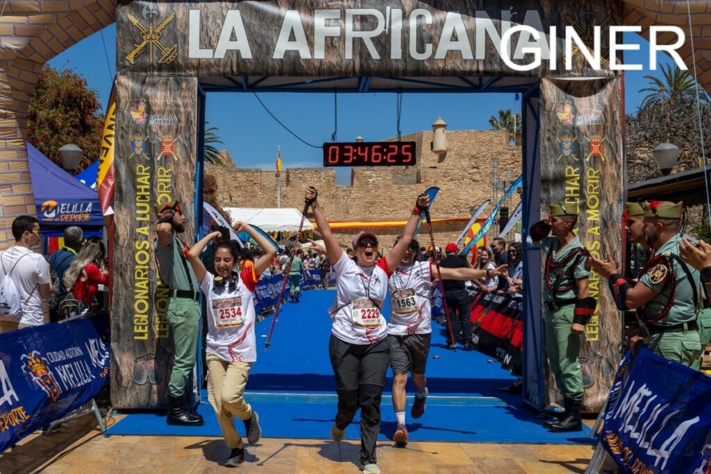 Runners celebrate crossing the finish line under a banner, timer reading 03:46:25, with cheering spectators nearby.