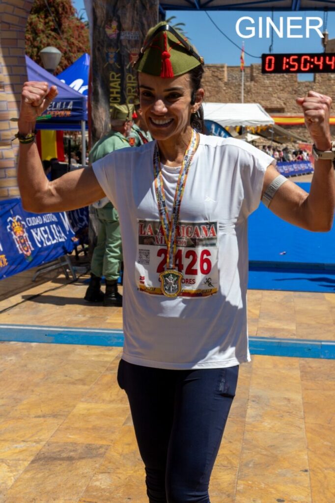Mujer sonriente con medalla en carrera, levantando los brazos.