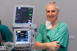 Cirujano sonriente en un entorno hospitalario con monitores médicos.