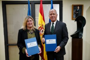 Dos personas sosteniendo documentos en un evento de firma de convenio en Melilla