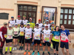Group of runners in colorful outfits posing on stairs with race bibs and sunglasses.