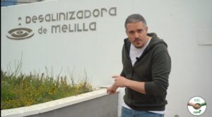 Hombre señalando la Desalinizadora de Melilla con flores alrededor.