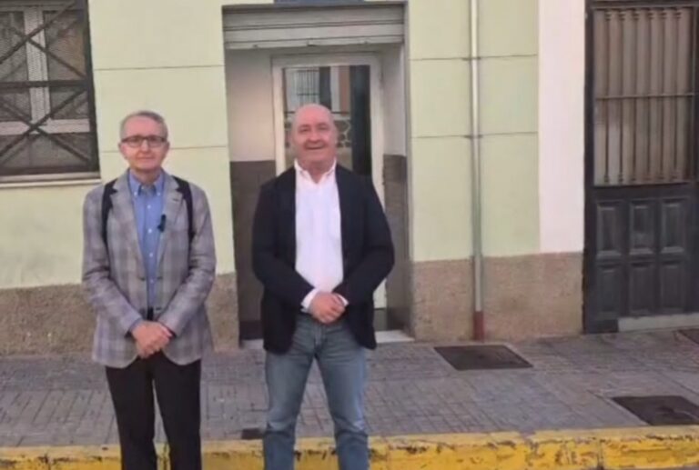 Dos hombres de pie frente a un edificio con puerta y ventanas.