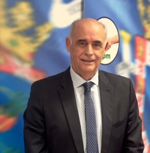 Professional man in a dark suit and polka-dot tie posing in front of a colorful backdrop with a world map design behind him