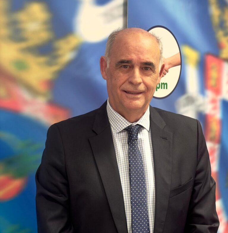 Professional man in a dark suit and polka-dot tie posing in front of a colorful backdrop with a world map design behind him