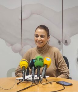 Mujer sonriente en una mesa con micrófonos de prensa
