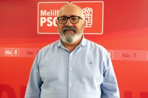 Retrato de un hombre con barba frente a un fondo rojo del PSOE