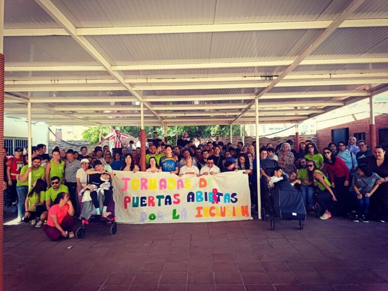 Group photo under a covered outdoor area with a colorful banner reading 'Jornadas Puertas Abiertas Por la Inclusión'