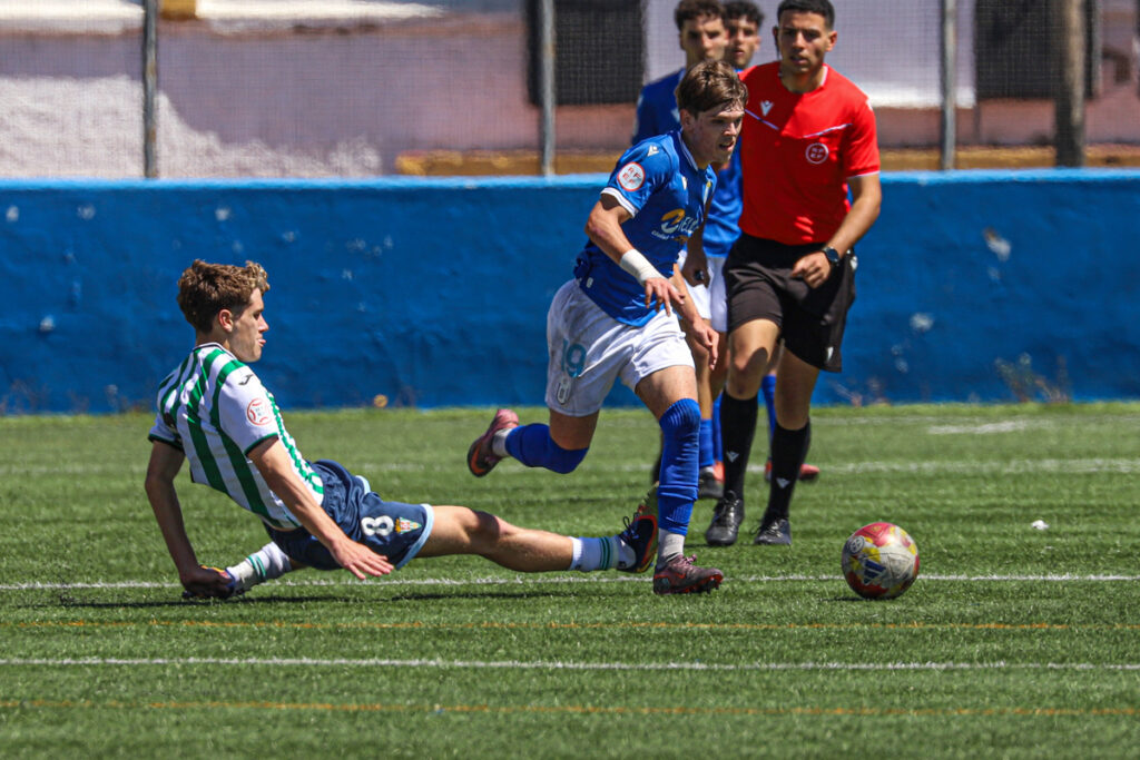 Jugador de fútbol cayendo mientras otro corre con el balón