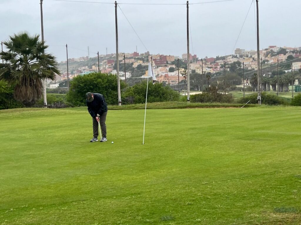 Jugador realizando un putt en un campo de golf bajo la lluvia en Melilla.