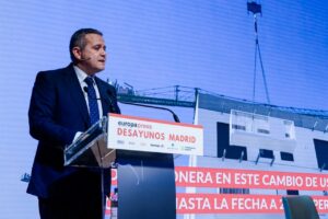 Man in a dark suit delivering a speech at a podium labeled 'Desayunos Madrid' during a Madrid conference event.