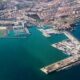 Aerial view of a seaside city with a large marina and multiple piers extending into turquoise water, viewed from above.