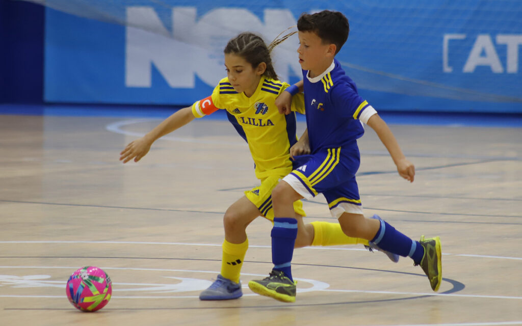 Dos niños jugando al fútbol sala en una cancha interior