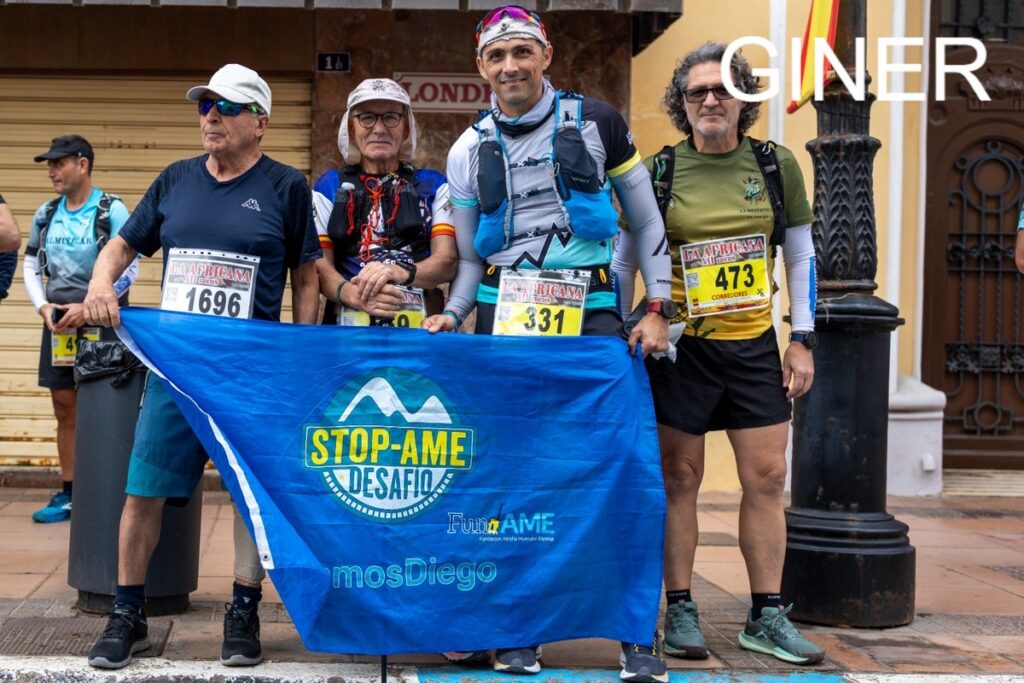 Group of five runners posing with a blue Stop-Ame Desafio banner on a city street, race bibs 1696 and 331 visible, upbeat mood overall.