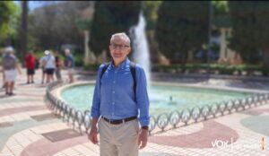 Hombre de pie junto a una fuente en un parque con personas al fondo