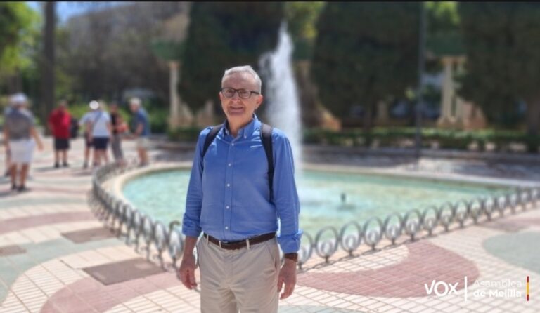 Hombre de pie junto a una fuente en un parque con personas al fondo