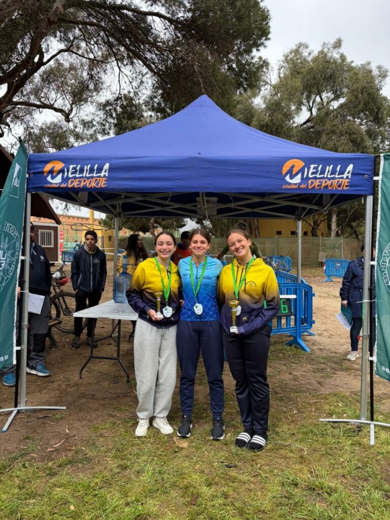 Tres ciclistas femeninas en el podio con medallas y trofeos