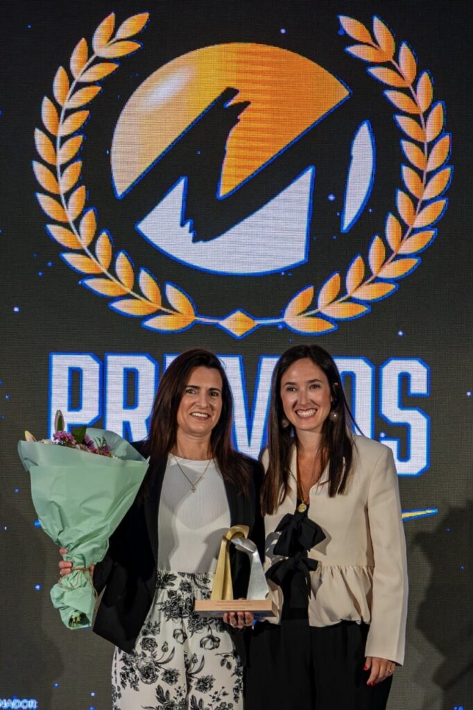 Dos mujeres sosteniendo un trofeo y un ramo de flores en un evento de premios.
