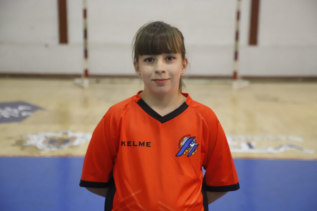 Niña en camiseta naranja de fútbol sala en un gimnasio