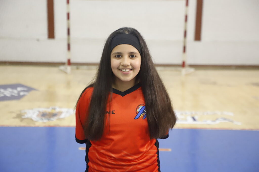 Niña sonriente con camiseta naranja en un campo de fútbol sala