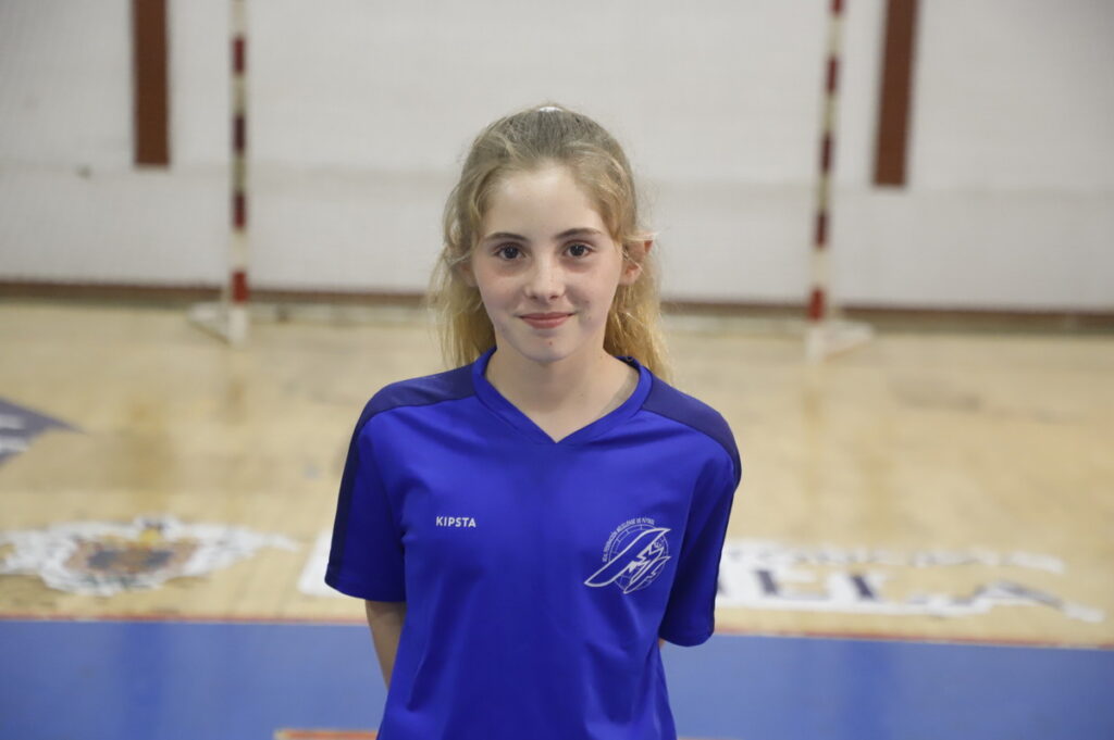 Niña sonriente con camiseta azul en una cancha de fútbol sala