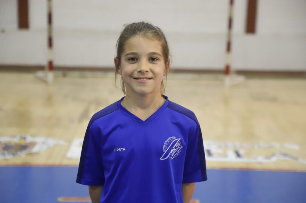 Niña sonriente en uniforme deportivo azul en un gimnasio