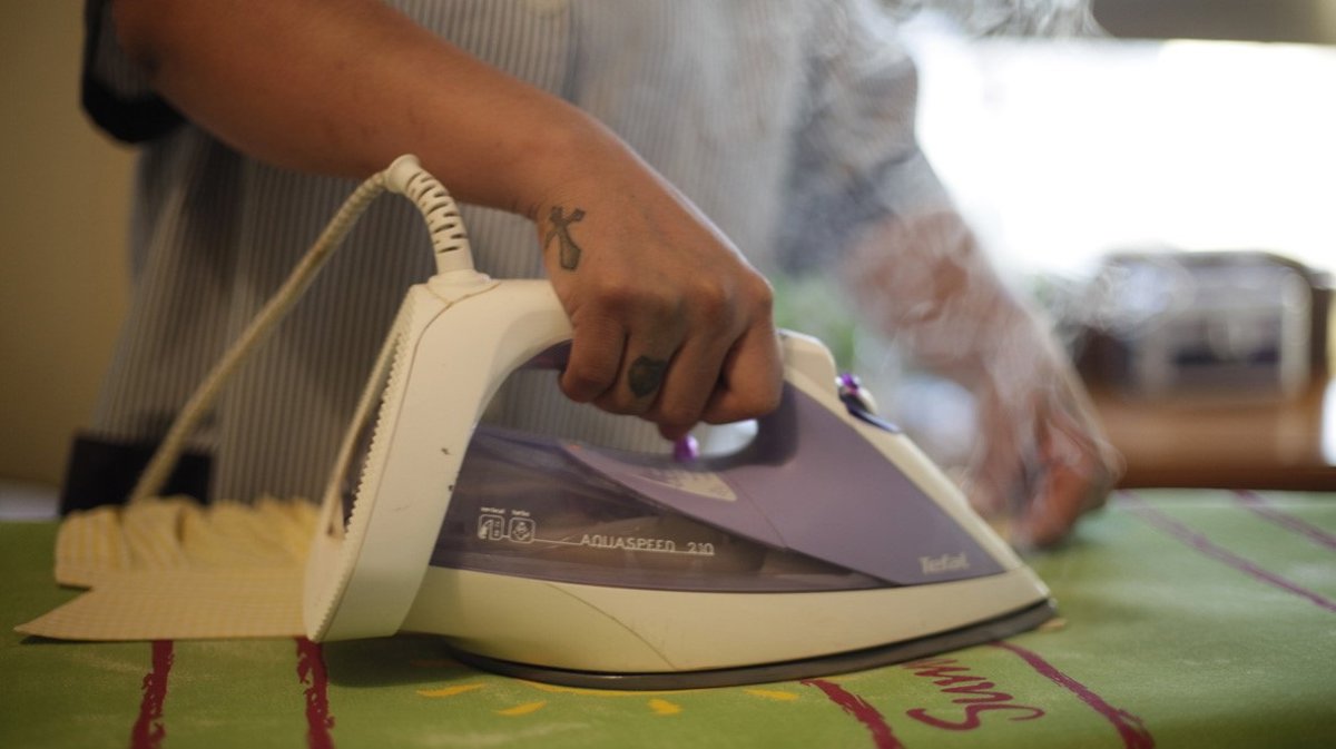 Mano de trabajadora del hogar usando una plancha en una tabla de planchar.