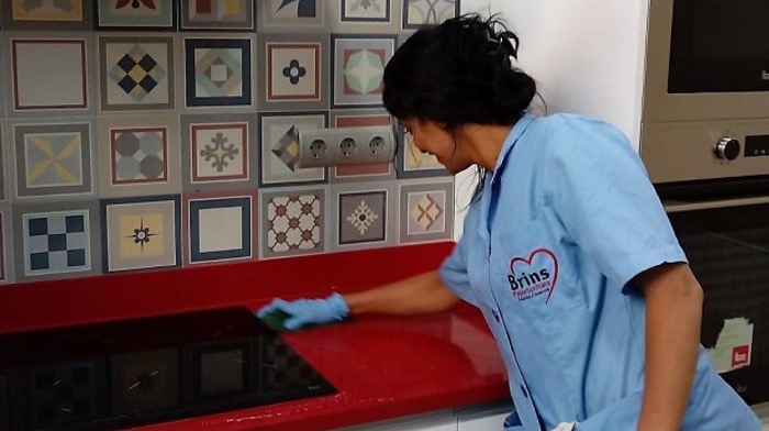 Trabajadora del hogar limpiando una cocina con guantes azules