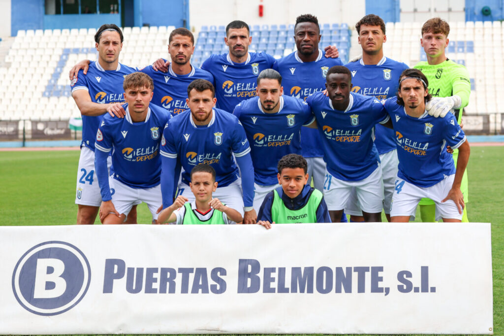 Equipo de fútbol U.D. Melilla posando en el campo con camiseta azul