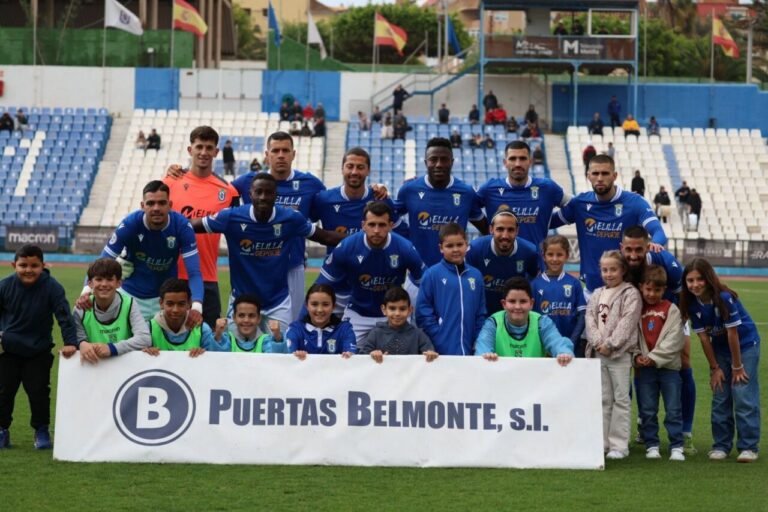 Jugadores de la U.D. Melilla posando con niños en el campo de fútbol