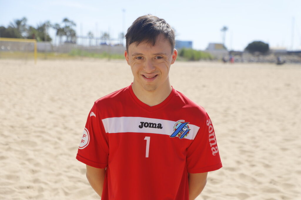 Jugador de fútbol playa de Melilla en camiseta roja sonriendo en la playa