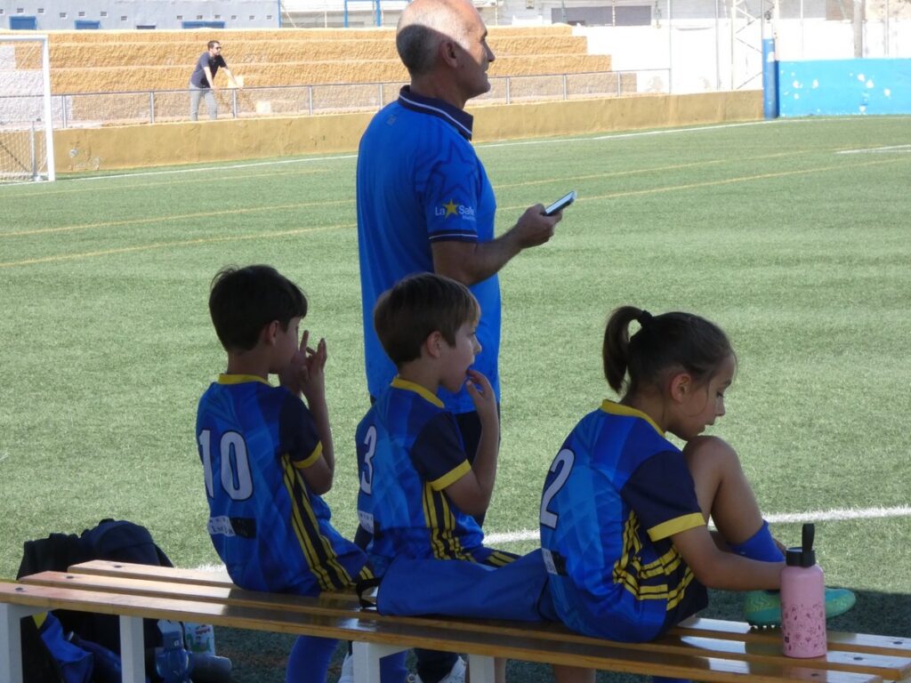 Niños y entrenador en el banquillo durante un torneo de fútbol infantil