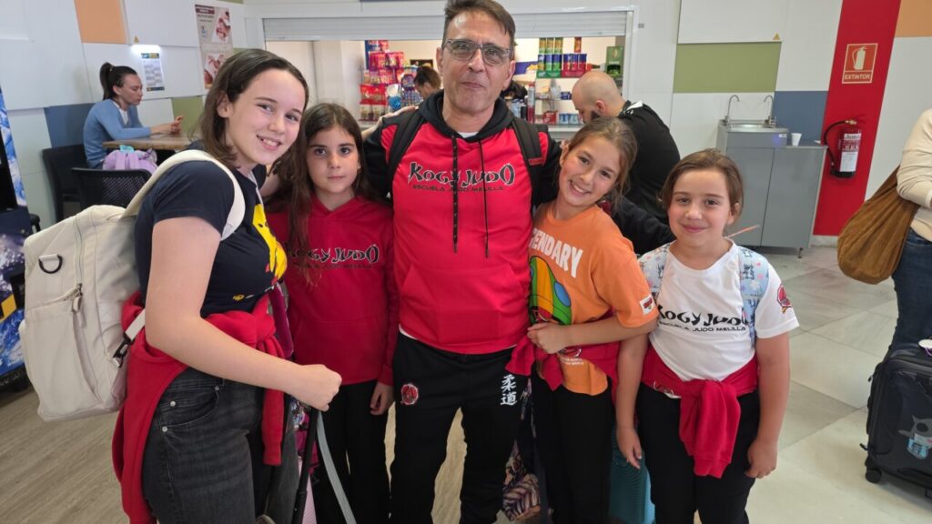 Man in a red hoodie posing with four smiling girls inside a shop.