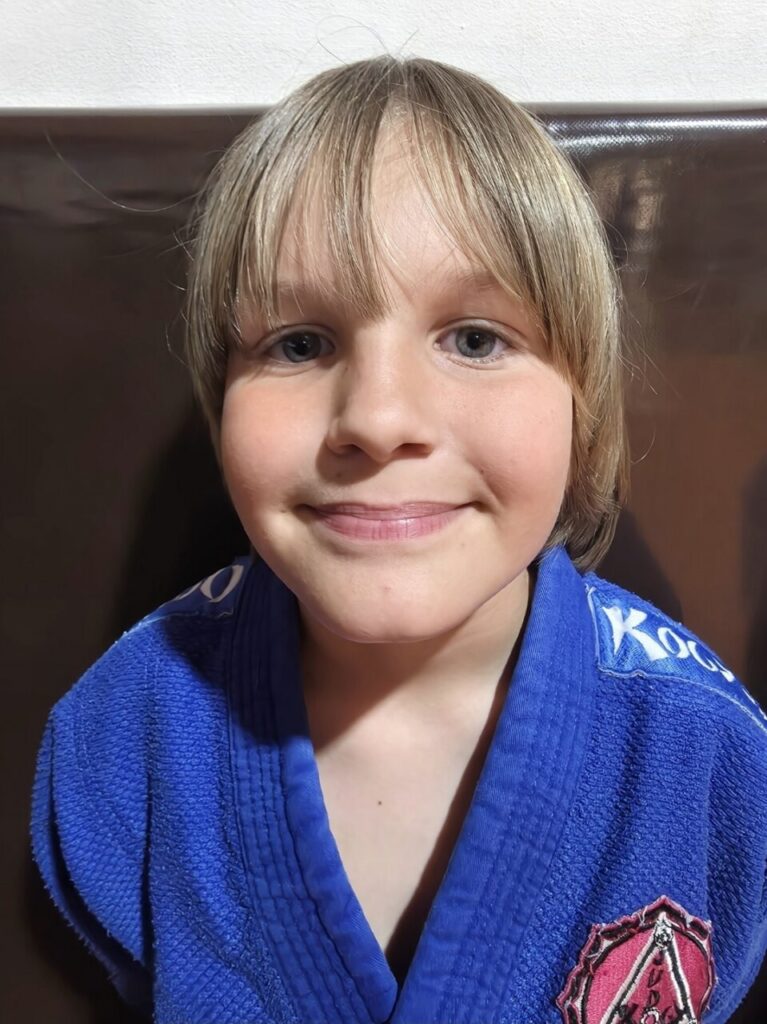 Young child with blond hair in a blue martial arts gi smiling at the camera