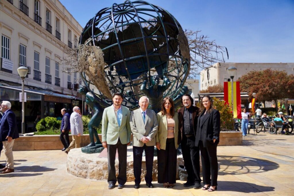 Five adults pose in front of a large metal globe sculpture in a sunny city plaza in a group photo.