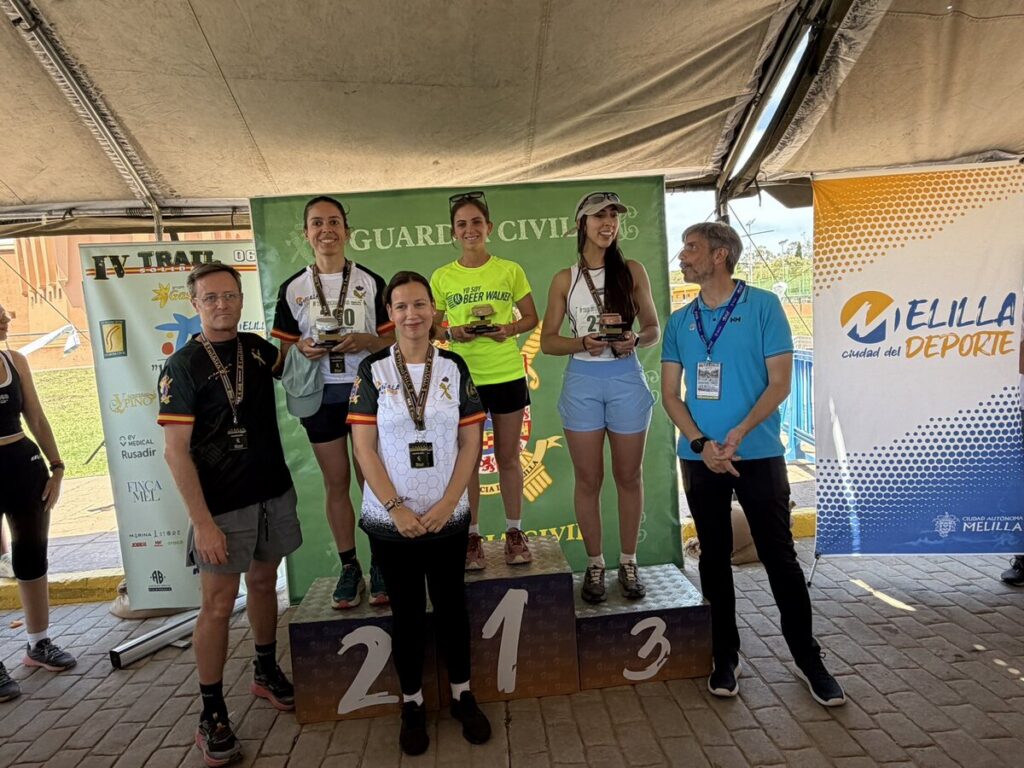 Group of female runners on a 1st–3rd place podium receiving medals during an award ceremony, with banners in the background.