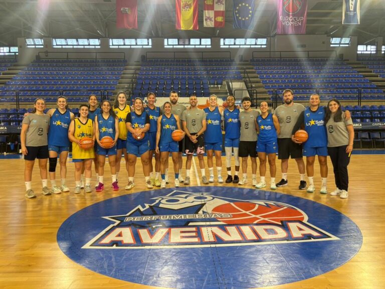 Basketball team posing on a wooden court in blue uniforms with a large Avenida logo on the floor.