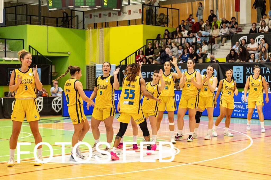 Women’s basketball team in yellow uniforms high-fiving on a basketball court after a game, with spectators watching from the stands.